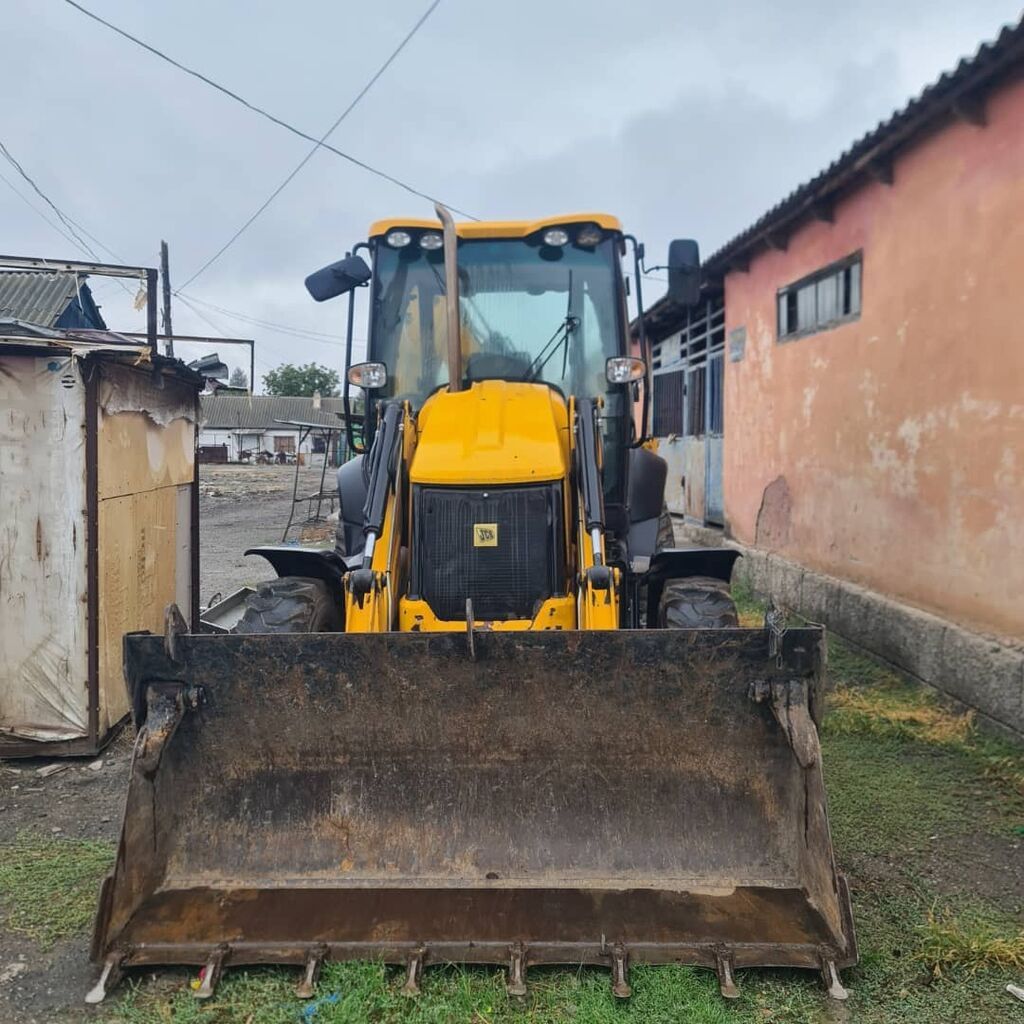Экскаватор-погрузчик JCB желтого цвета.Машина имеет кабину оператора с